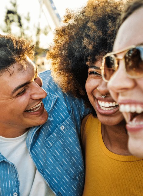 Three diverse young friends laugh joyfully together outdoors during Spring Break, with curly-haired woman in sunglasses at centre, evoking fun group travel vibes for Dublin hostel stays.