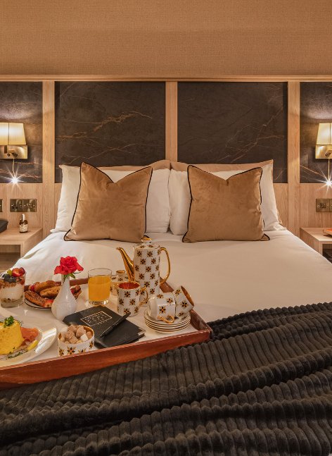 A stylish County Arms bedroom with a large double bed, tray of breakfast on the bed, and warm elegant décor.