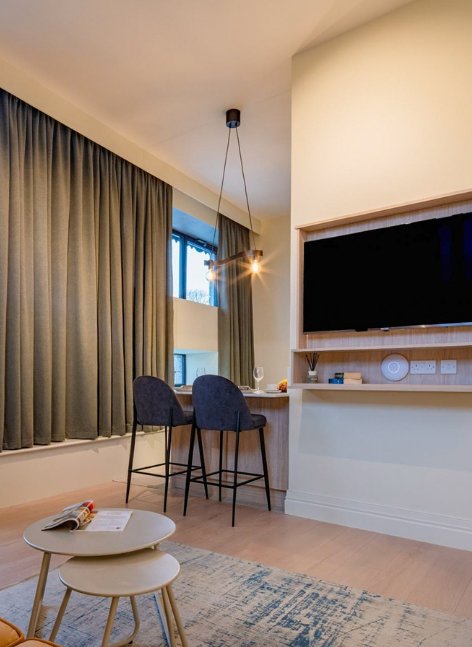 Contemporary hotel room in The Malt Store in Birr with a wall mounted TV, high stools at a compact desk, floor to ceiling curtains and a seating area.