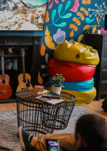 Living room with some guitars, colourful bean-bags, a guest using their mobile and watching TV at Gardiner House Hostel in Dublin