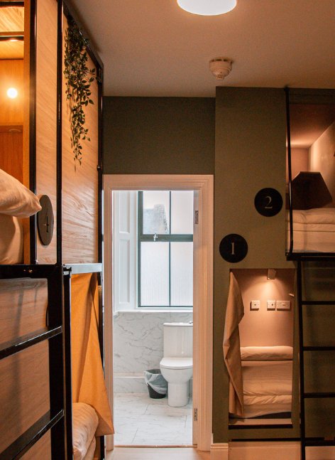 Inside Gardiner House Hostel dorm room with bunk beds on both sides, a private bathroom visible through the open doorway, and warm modern lighting.