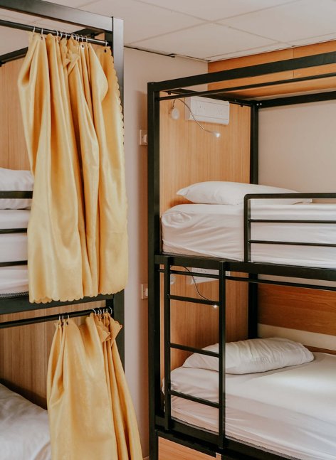 A clean Garden Lane Backpackers dorm room with bunk beds, privacy curtains, and warm wooden wall panels.