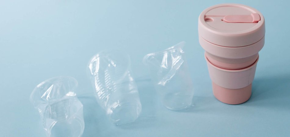 Three plastic disposable cups followed by a reusable cup to make people reflect about single-use plastics