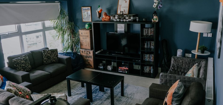 Two girls in a cosy living room, one playing guitar, the other one reading beside the book shelf. 