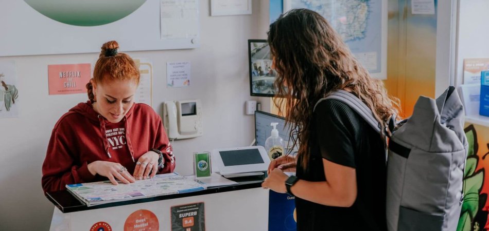 Two girls, talking over the counter at a hostel reception